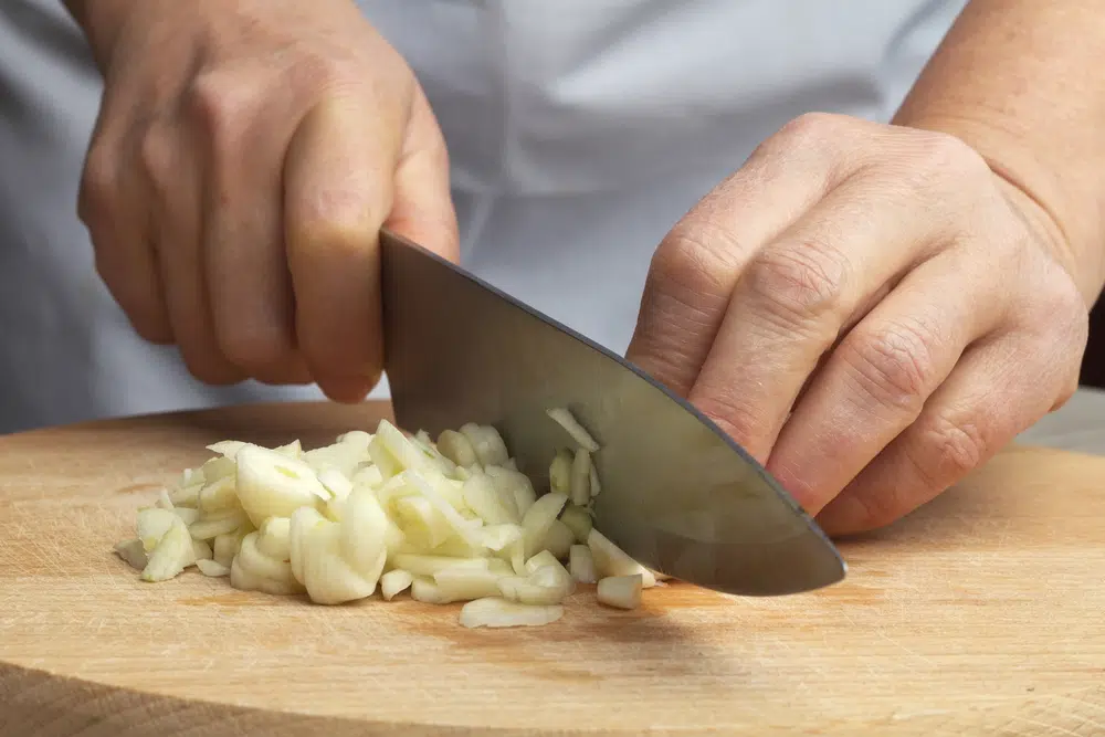 Person Mincing Garlic On A Wooden Chopping Board