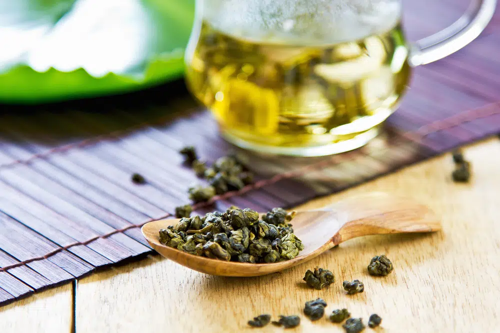 Oolong Tea Leaf On A Wooden Spoon With A Glass Of Oolong Tea On The Background