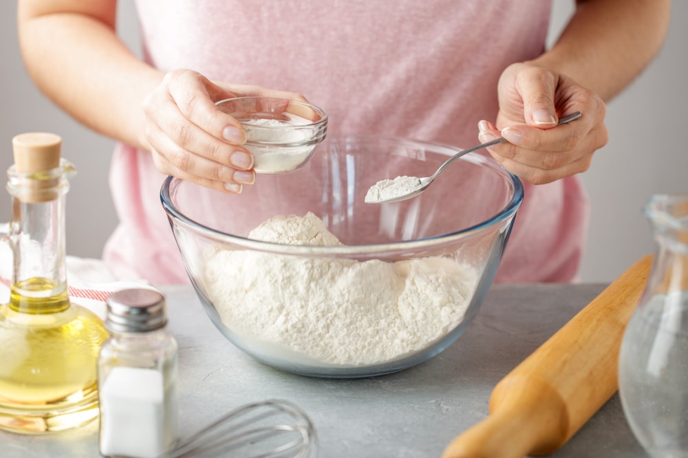 Woman adds the baking powder into the glass bowl with flour