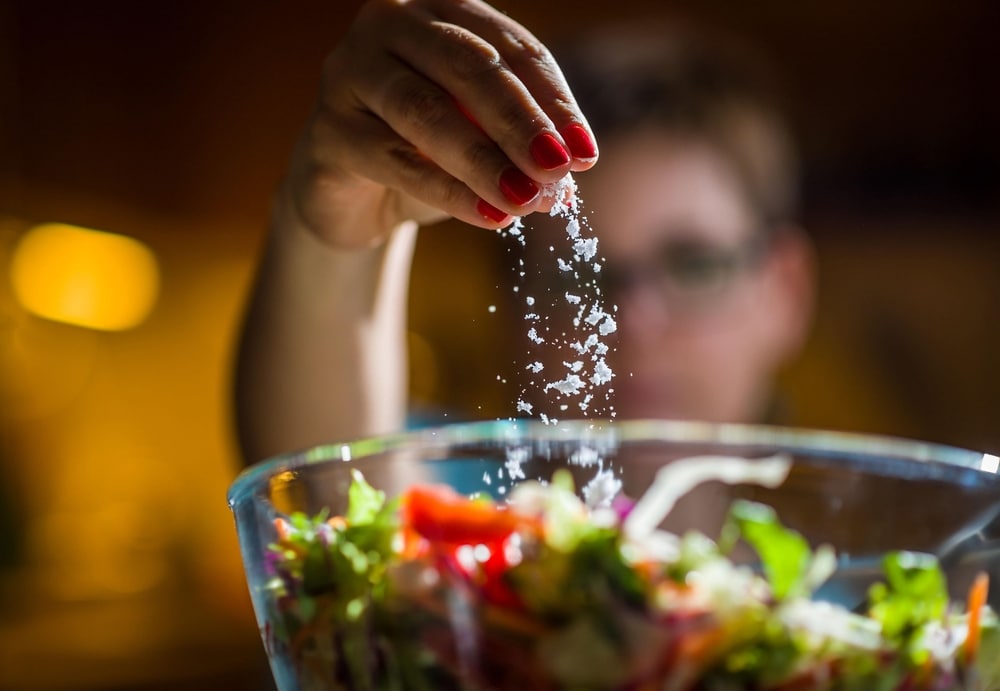 Frau bereitet gesunden Salat zu und fügt der Schüssel Salz hinzu