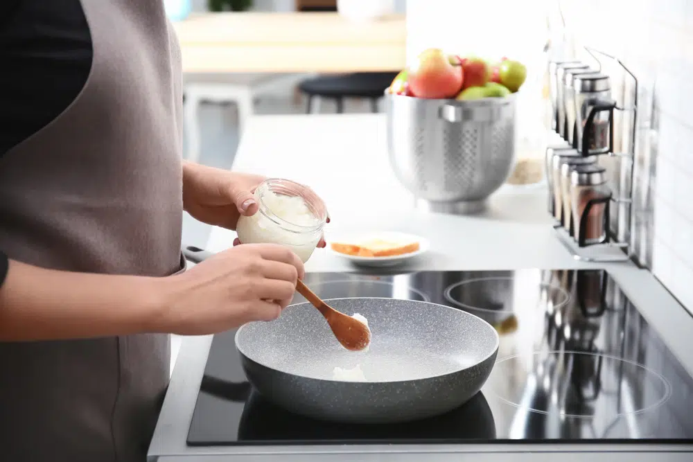 Woman Putting Coconut Oil On Frying Pan While In Kitchen