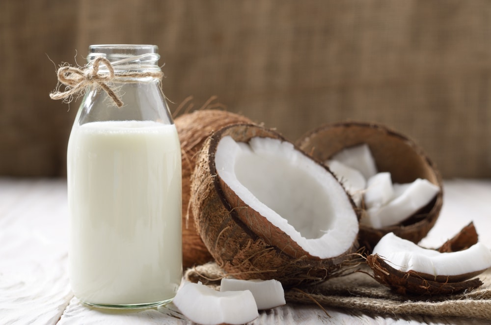 A Bottle Of Coconut Milk With Coconuts Beside It