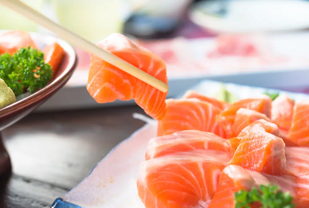 Chopstick Picking Up A Piece Of Salmon Sashimi From A Set