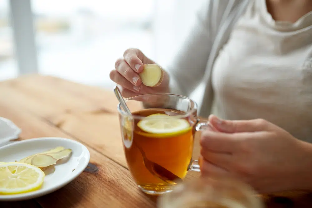 Close Up Of Woman Adding Ginger To Lemon Tea