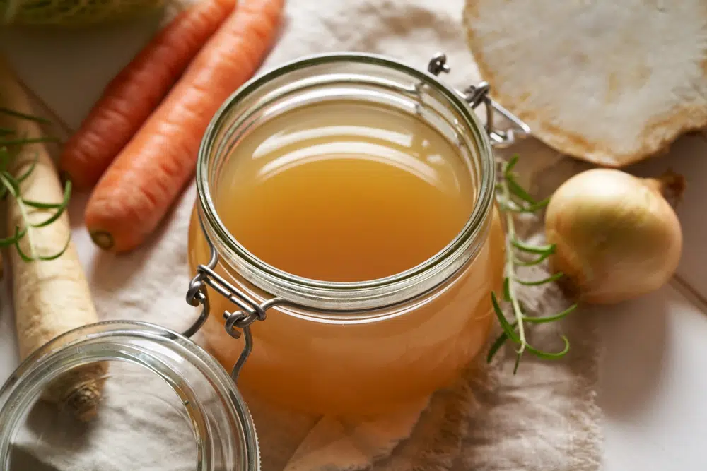 Homemade Pho Broth In A Glass Jar, With Vegetables On The Background