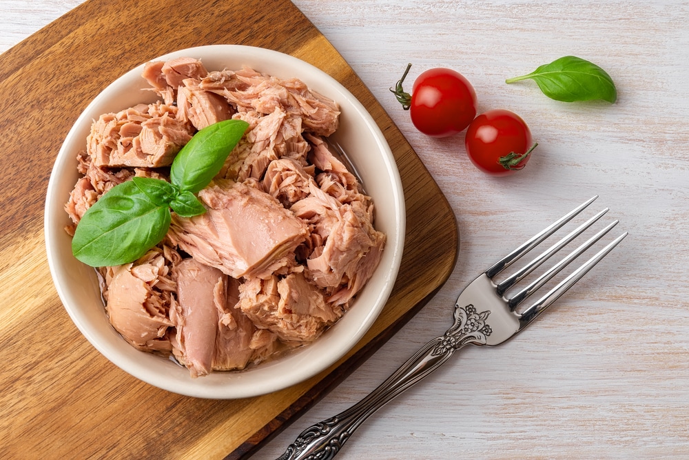 Top View Of Canned Tuna In A Bowl, Fork And Red Cherry Tomatoes On A White Wooden Table