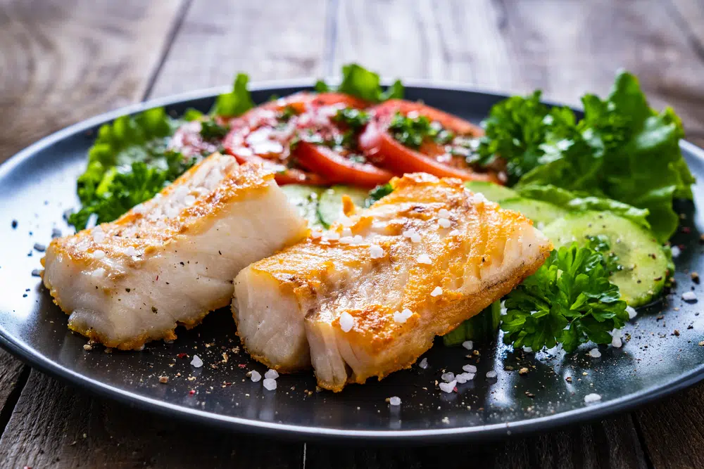 Fried Cod Fillet With Vegetables On Wooden Table